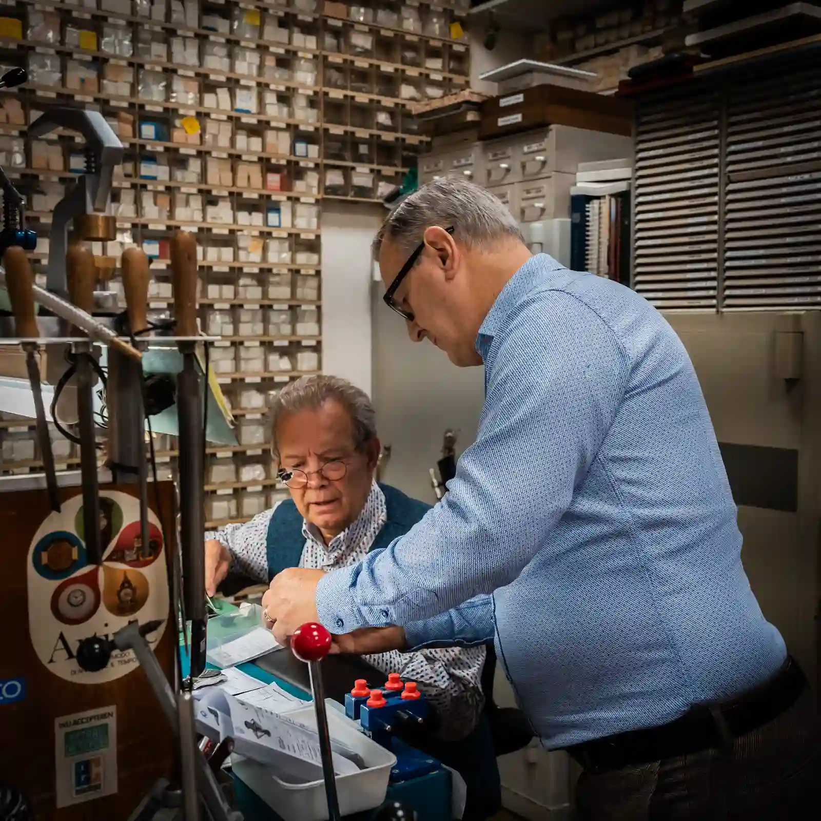 Twee klokkenmakers bespreken een uurwerk aan de werkbank in het atelier